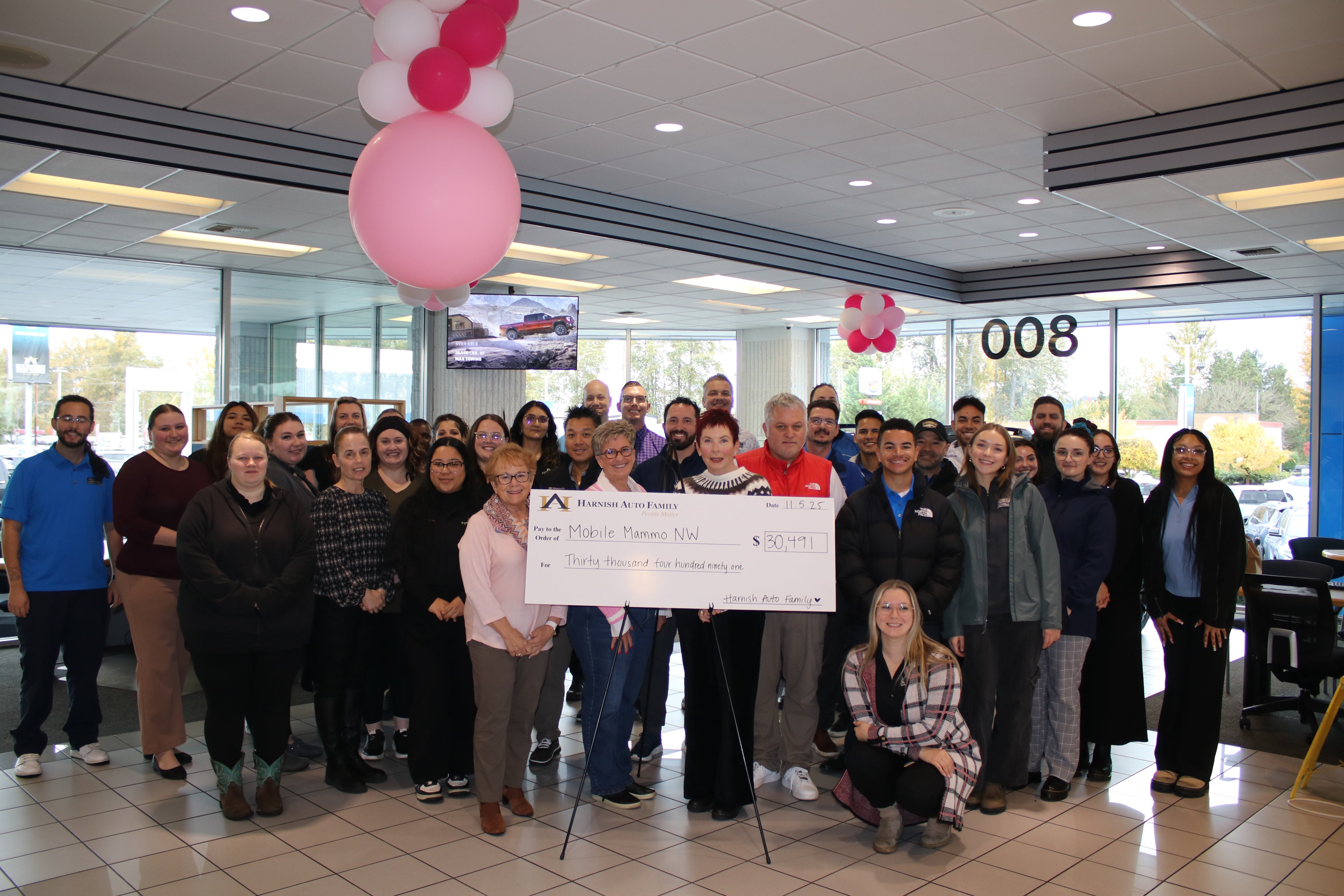 A large group of people smiling, gathered around a giant check for $30,491 made out to Mobile Mammo NW from Harnish Auto Family.