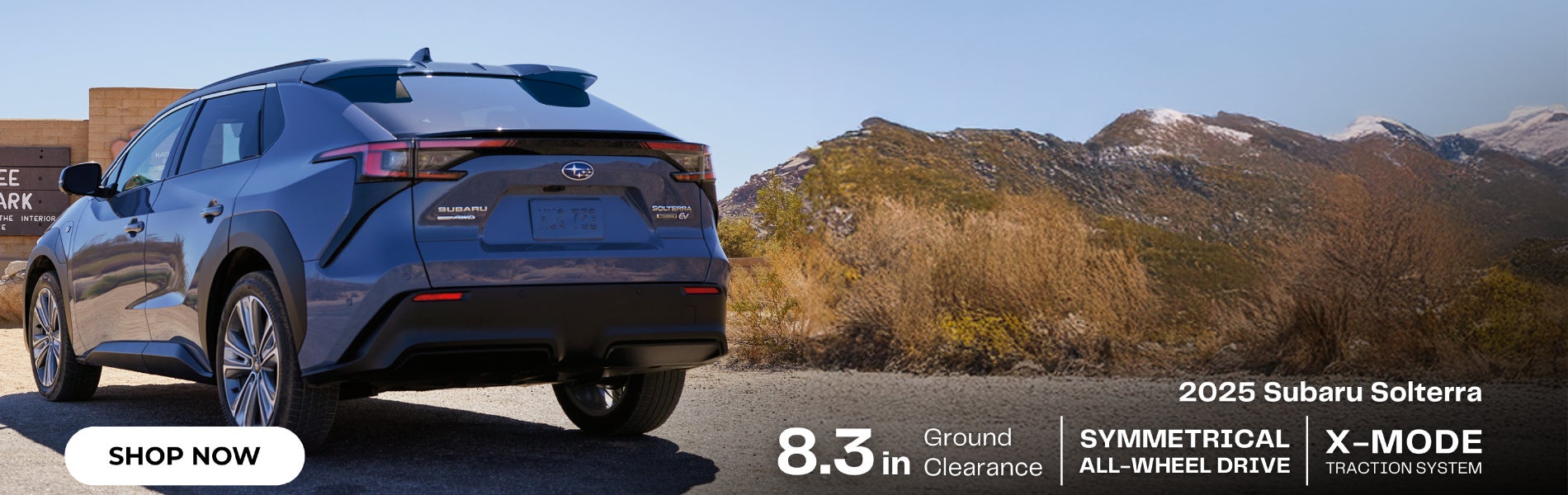 Rear view of a dark blue 2025 Subaru Solterra SUV parked in a desert landscape with mountains in the background.