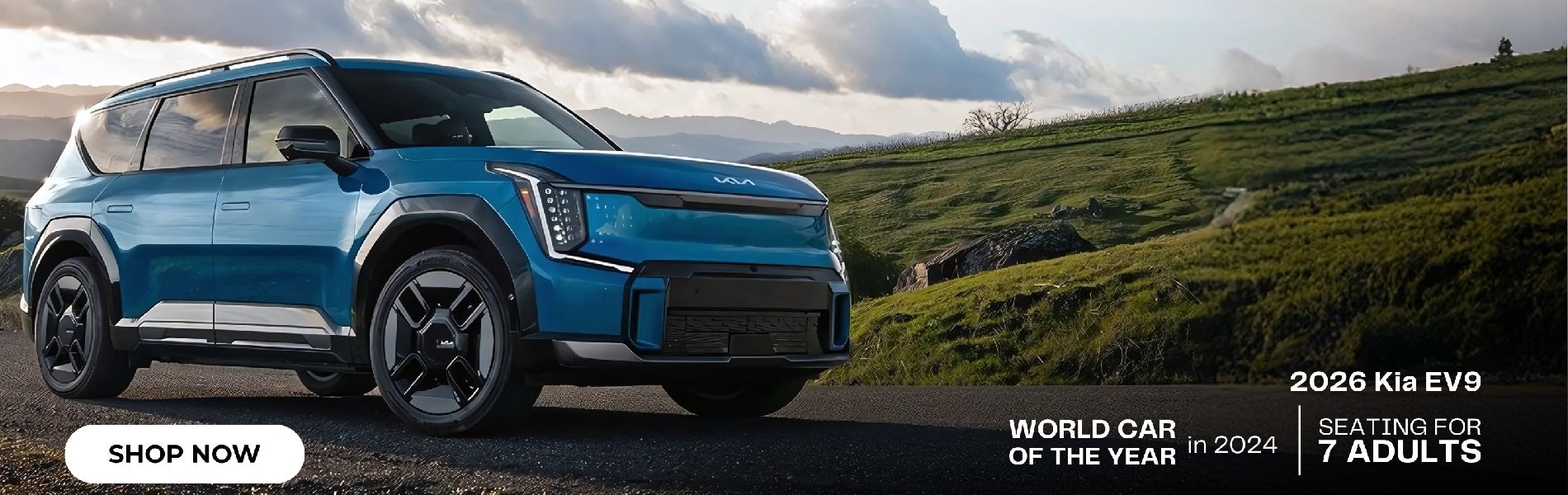 Blue 2026 Kia EV9 parked on a hilly road under a cloudy sky next to text WORLD CAR OF THE
YEAR in 2024.
