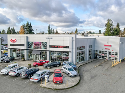 Aerial view of the modern Kia of Everett dealership building with multiple new cars in its parking lot.