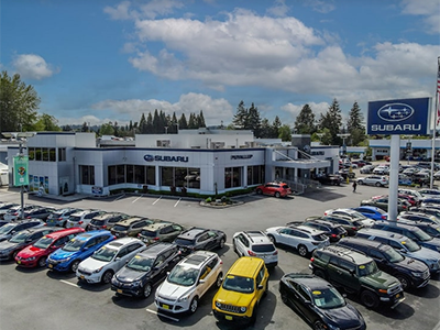 Aerial view of a sprawling Subaru dealership with dozens of cars in the lot under a bright blue sky