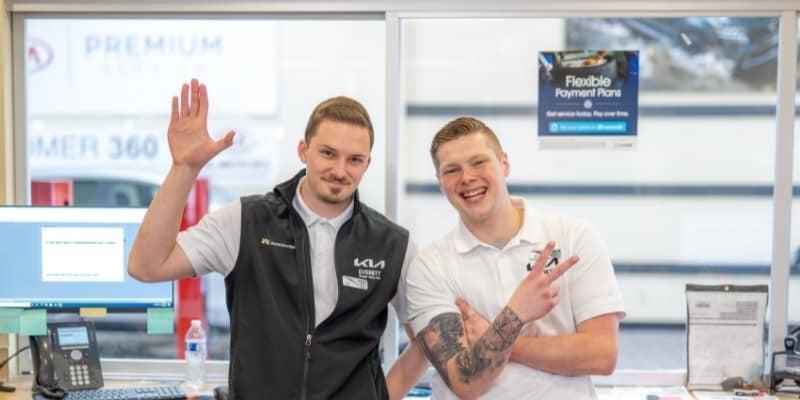 Two Harnish Auto Family employees smiling and welcoming customers inside a dealership showroom.